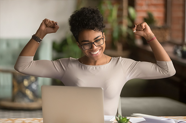 African American woman celebrating at computer after passing real estate exam.